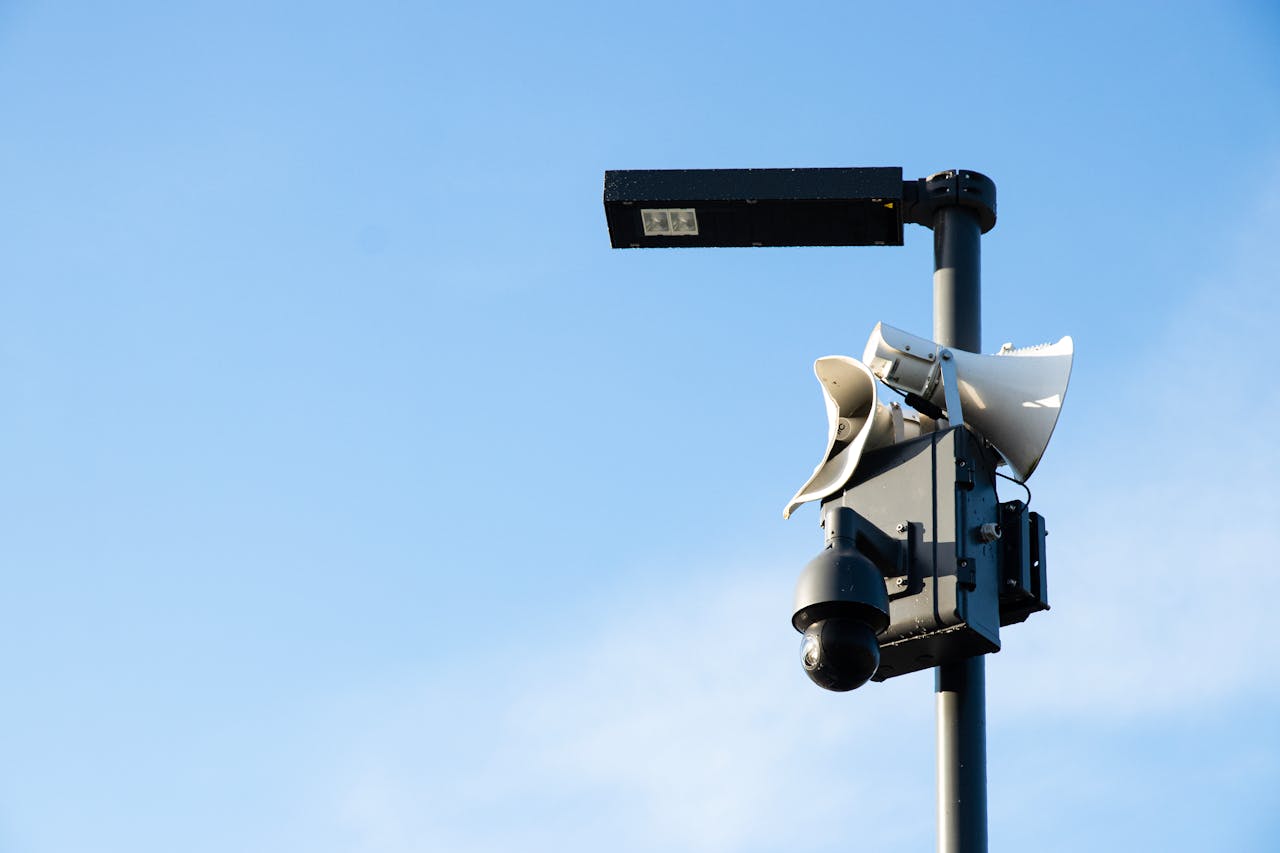 Street lamp post with security camera and speakers under a blue sky in Jūrmala, Latvia.